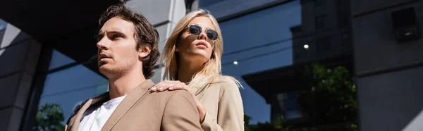 Low angle view of blonde woman in sunglasses looking away near man on street, banner — Stock Photo