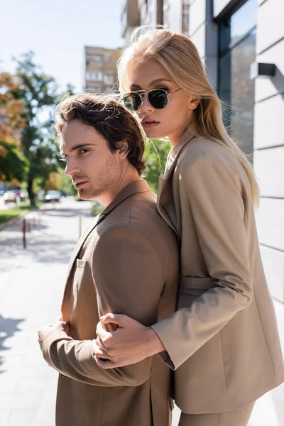 Jeune femme dans des lunettes de soleil élégantes étreignant l'homme brune en plein air — Photo de stock