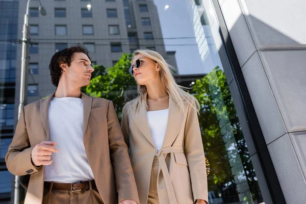 Low angle view of young couple in beige blazers looking at each other outdoors — Stock Photo