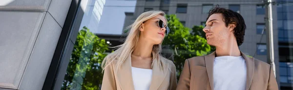 Низкий угол зрения на молодого человека и блондинку в солнечных очках глядя друг на друга на открытом воздухе, баннер — стоковое фото