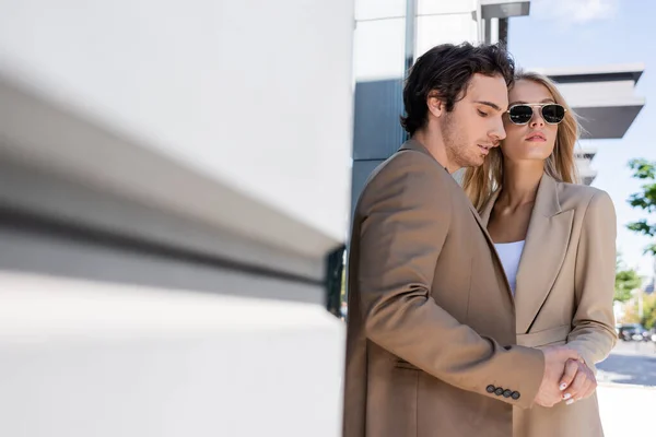 Trendy junges Paar hält Händchen nahe verschwommener Mauer im Freien — Stockfoto