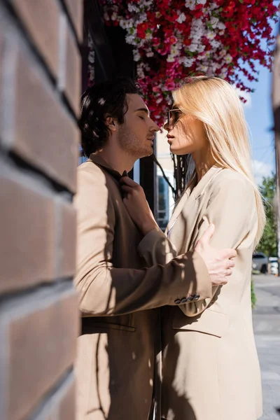 Vista laterale di uomo bruna e donna bionda in occhiali da sole in piedi faccia a faccia vicino alla parete offuscata — Foto stock