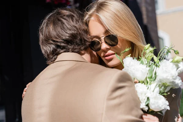 Donna bionda in occhiali da sole con bouquet di eustoma bianco vicino al giovane — Foto stock