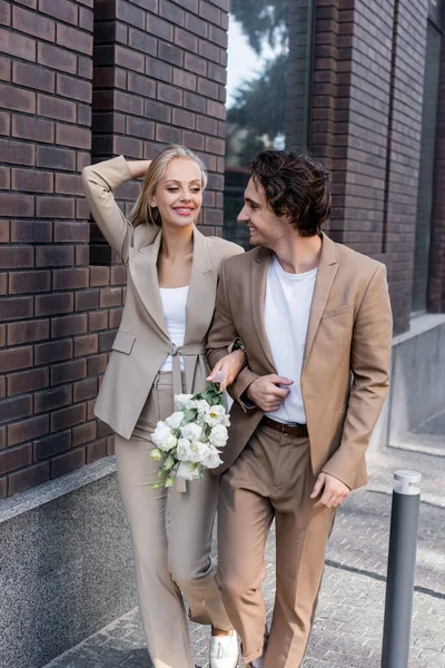 Happy woman with bouquet looking at boyfriend while walking in city — Stock Photo