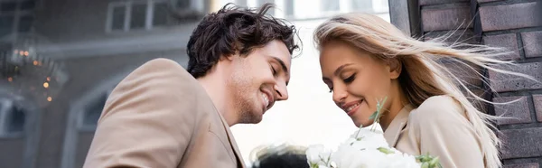 Baixo ângulo vista de feliz jovem casal sorrindo perto de buquê branco ao ar livre, banner — Fotografia de Stock