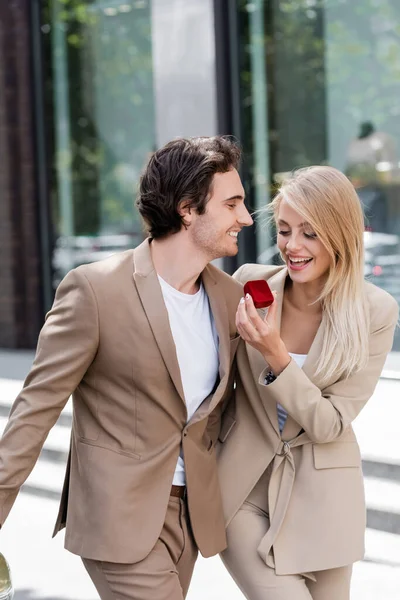 Amazed blonde woman holding jewelry box near young man on city street — Stock Photo