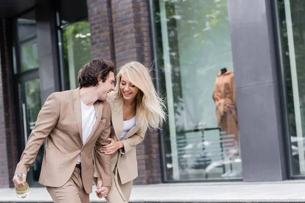 Aufgeregtes Paar hält Händchen, während es mit Champagnerflasche auf der Straße spaziert — Stockfoto