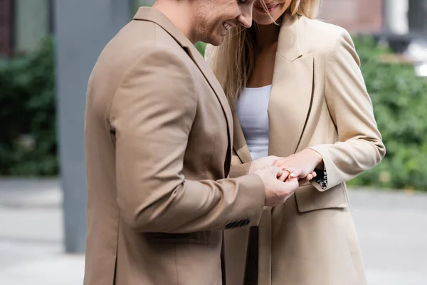 Vista cortada de homem feliz colocando anel de casamento no dedo da mulher ao ar livre — Fotografia de Stock