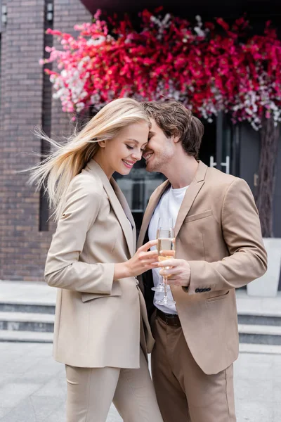 Pretty blonde woman clinking champagne glasses with boyfriend on street — Stock Photo