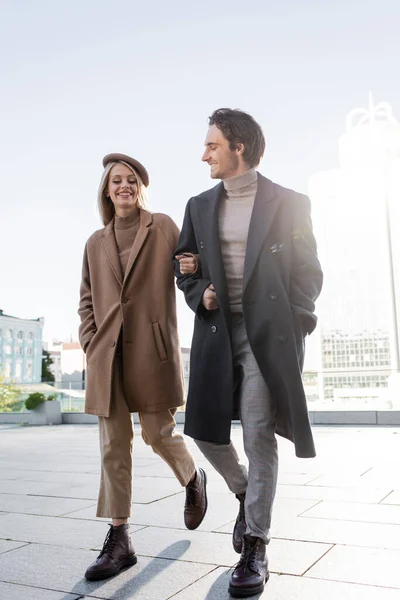 Full length of young couple in coats and leather boots walking in city — Stock Photo