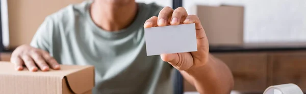 Ausgeschnittene Ansicht eines afrikanisch-amerikanischen Verkäufers mit Visitenkarte in der Nähe des Pakets im Geschäft, Banner — Stockfoto