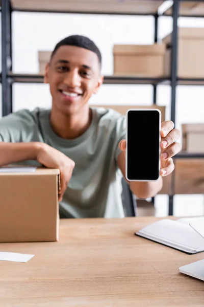 Blurred african american online web store owner holding smartphone near carton box — Stock Photo