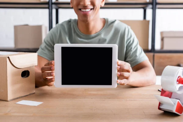 Vista ritagliata del venditore africano americano sorridente che tiene il tablet digitale vicino al nastro adesivo e alla scatola di cartone — Foto stock