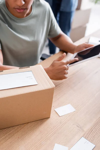 Vista recortada del vendedor afroamericano utilizando tableta digital cerca de la caja de cartón en la tienda web en línea - foto de stock