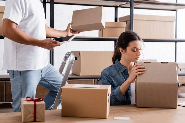 Young seller holding carton box near african american colleague with digital tablet in store — Stock Photo