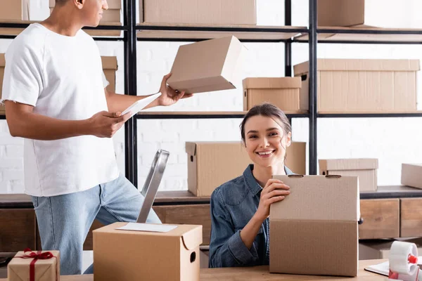 Positivo venditore contenente scatola di cartone vicino al collega afro-americano con tablet digitale in negozio — Foto stock