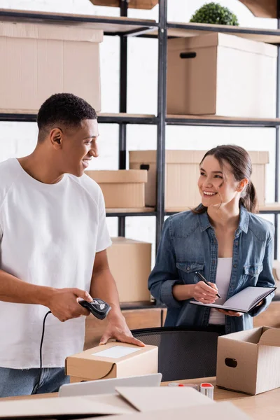 Fröhliche gemischtrassige Verkäufer scannen Paket und halten Laptop in Online-Webshop — Stockfoto