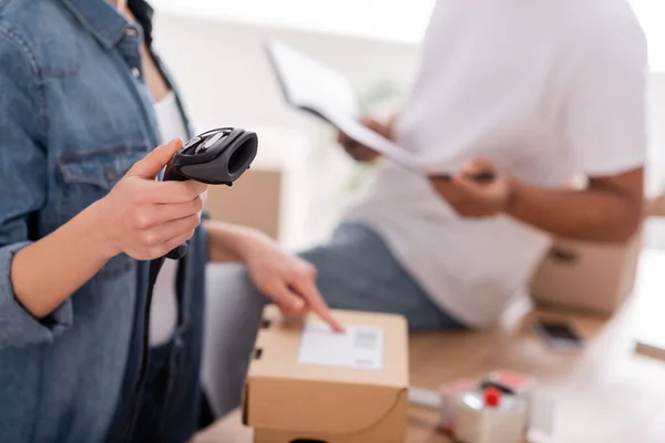 Ausgeschnittene Ansicht des Verkäufers mit Scanner in der Nähe verschwommener afrikanischer Kollege und Paket im Geschäft — Stockfoto