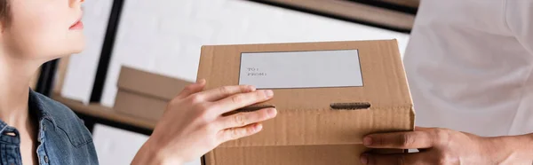 Cropped view of interracial sellers holding carton box with shipping label in online web store, banner — Stock Photo