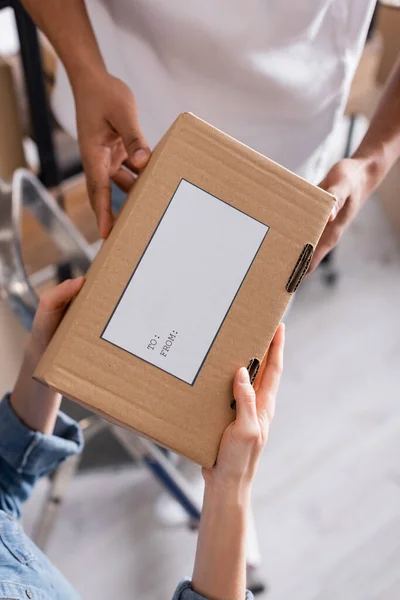 Vista recortada de vendedores multiétnicos sosteniendo caja de cartón con etiqueta de envío en tienda web en línea - foto de stock