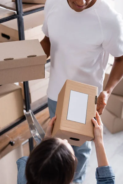 Vista aérea de los vendedores multiétnicos que sostienen el paquete con la etiqueta del envío en la tienda en línea del Web - foto de stock