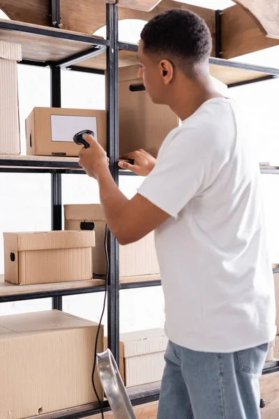 Vista lateral de los paquetes de escaneo del propietario de la tienda web en línea afroamericana en rack - foto de stock