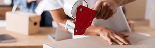 Cropped view of african american seller holding adhesive tape near carton box in online web store, banner — Stock Photo