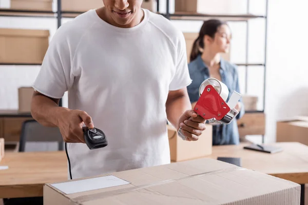 Paquete de escaneo de vendedor afroamericano y celebración de cinta adhesiva en la tienda web en línea - foto de stock