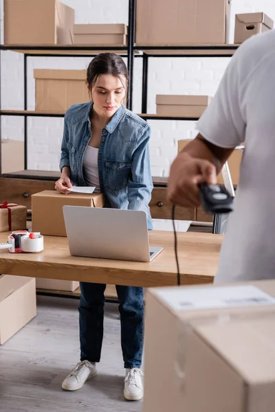 Seller holding shipping label near packages and laptop in online web store — Stock Photo