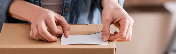 Cropped view of online web store owner fastening shipping label on carton box, banner — Stock Photo