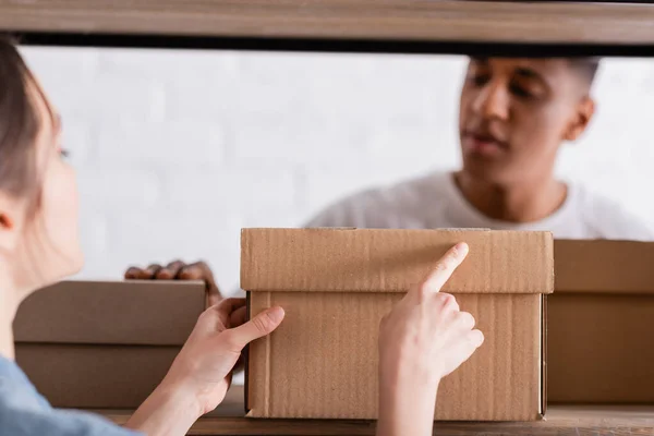 Seller pointing at carton box near blurred african american colleague in online web store — Stock Photo