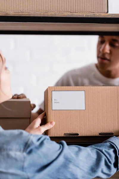 Blurred vendedor celebración de caja de cartón cerca borrosa africana colega americano en la tienda web en línea - foto de stock