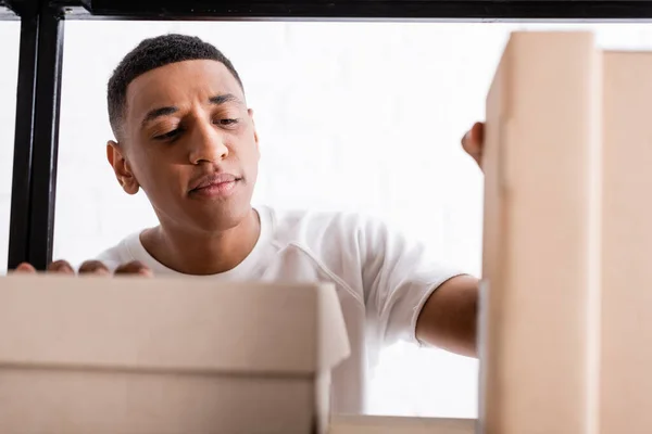 African american online web store owner looking at cardboard boxes on rack — Stock Photo