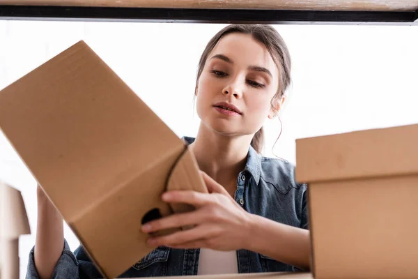 Jeune vendeur tenant boîte de carton près de rack dans la boutique en ligne — Photo de stock