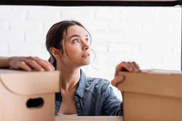 Proprietário da loja online olhando para longe perto de caixas de papelão borradas no rack — Fotografia de Stock