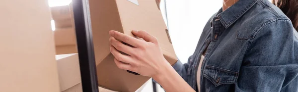 Cropped view of seller holding carton box near rack in online web store, banner — Stock Photo