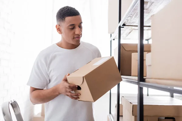 African american seller holding package near rack in online web store — Stock Photo
