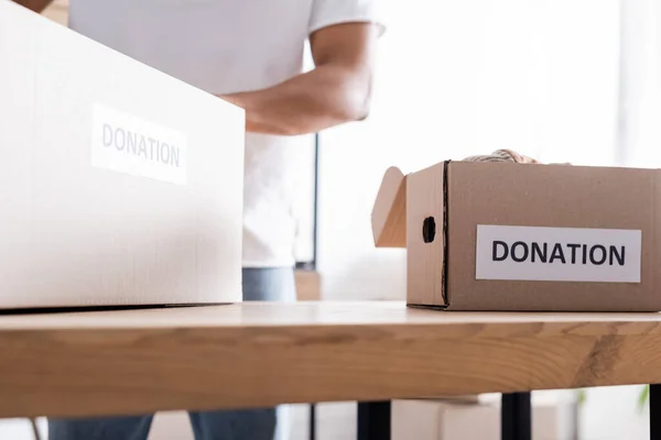 Cropped view of boxes with donation lettering near blurred african american owner of online web store — Stock Photo