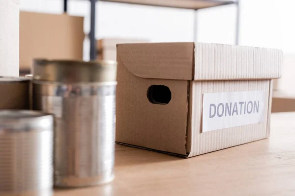Box with donation lettering near blurred canned food on table — Stock Photo