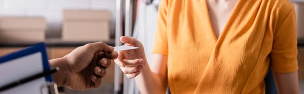 Cropped view of african american deliveryman holding business card near seller in online web store, banner — Stock Photo