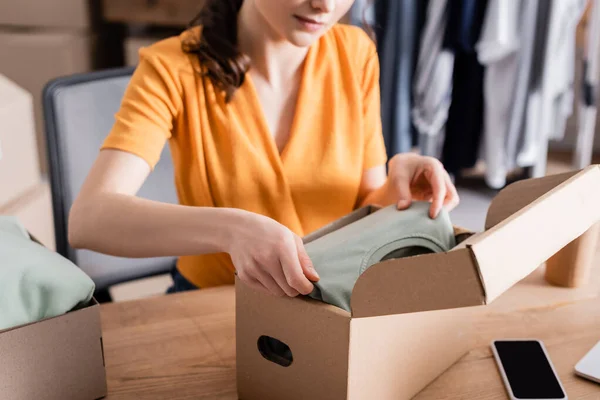 Vue recadrée du propriétaire mettre des vêtements dans la boîte dans la boutique en ligne — Photo de stock