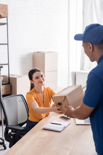 Smiling proprietor giving box to african american courier in online web store — Stock Photo