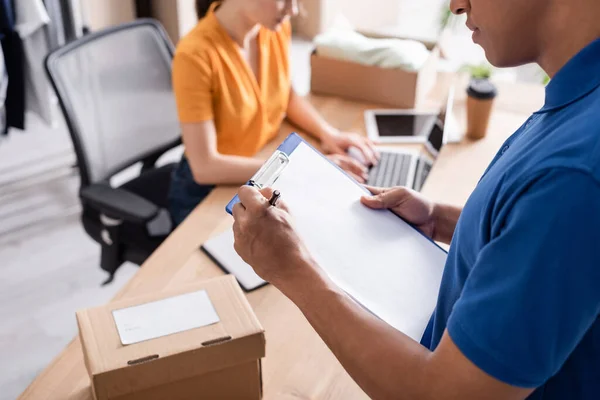 Cropped view of african american courier writing on clipboard in online web store — Stock Photo