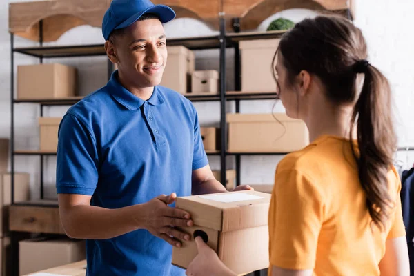 Sorrindo Africano americano entregador tomando caixa de papelão do proprietário na loja online — Fotografia de Stock