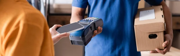 Cropped view of proprietor paying with smartphone near african american courier in online web store, banner — Stock Photo