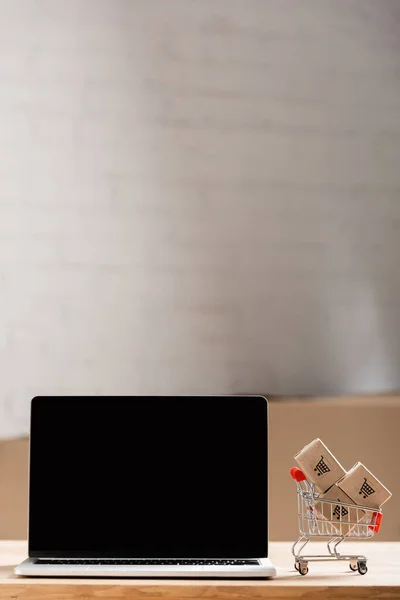 Laptop with blank screen near toy shopping cart and packages on table — Stock Photo