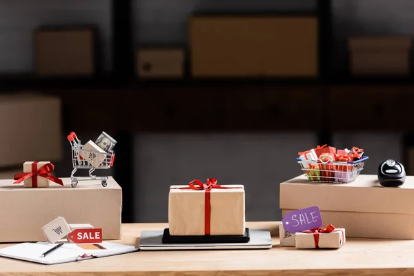 Подарочные коробки, ноутбук и корзина с деньгами на столе — стоковое фото
