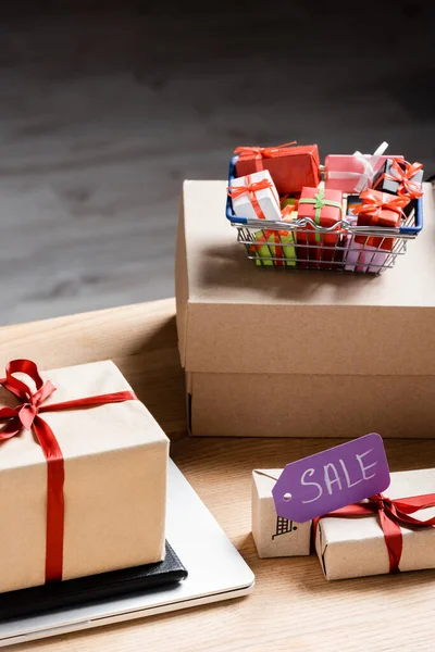 Price tag with sale lettering near toy gift boxes and laptop on table — Stock Photo