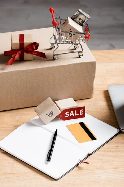 Price tag with sale lettering near credit card, notebook and carton box on table — Stock Photo