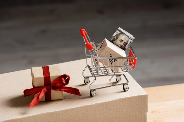 Toy cart with money near gift box and package on table — Stock Photo